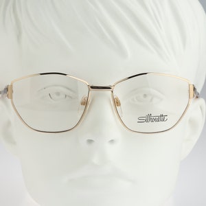 Könnte beinhalten: Goldfarbene Metallbrille mit dem Markennamen Silhouette auf der rechten Linse.