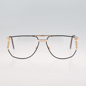 Könnte beinhalten: Brille mit einem dünnen schwarzen Drahtrahmen und einem Doppelsteg-Design. Die Bügel und Stegakzente sind in einem metallischen Goldton gehalten, mit horizontalen Rillendetails an den Außenkanten des Rahmens in der Nähe der Scharniere.