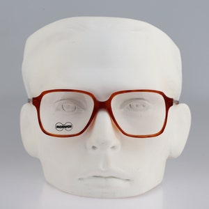 May include: Brown tortoiseshell eyeglasses with clear lenses. The glasses have a square frame and the brand name "MORWEN" is printed on the left lens.