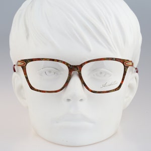 Puede incluir: Un par de gafas marrones y doradas con un patrón floral en el marco. El nombre de la marca "Annabella" está impreso en la lente derecha.