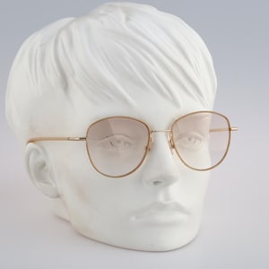 May include: A gold-rimmed pair of glasses with light brown lenses on a white mannequin head.