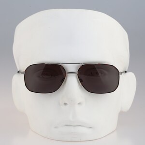 May include: Silver aviator sunglasses with dark brown lenses. The sunglasses are on a white mannequin head.