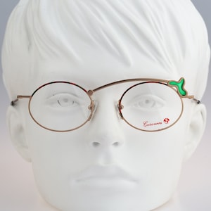 May include: Gold-rimmed round eyeglasses with a green accent on the right temple arm. The brand name "Casanova" is printed in red on the right lens.