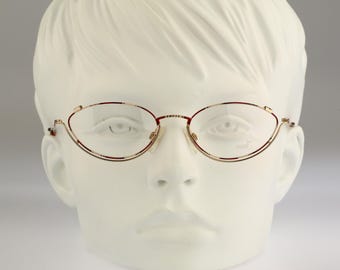 Könnte beinhalten: Ovale Brille mit einem dünnen, goldfarbenen Metallrahmen. Die Brille verfügt über klare Gläser und ein filigranes Stegdesign. Der Rahmen hat eine subtile, raffinierte Struktur, die der ovalen Form der Gläser folgt und für einen klaren Look sorgt.