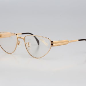 May include: Gold-tone metal eyeglasses with a cat-eye frame and clear lenses. The brand name "Silhouette" is printed on the right temple.