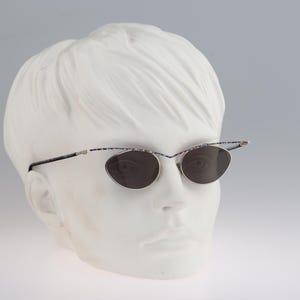 May include: A pair of silver-rimmed sunglasses with dark lenses and a colorful pattern on the arms. The sunglasses are on a white mannequin head.