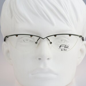 Könnte beinhalten: Eine Brille ohne Rahmen in Schwarz und Gold mit einem Flair Jet Set Logo auf der rechten Linse.
