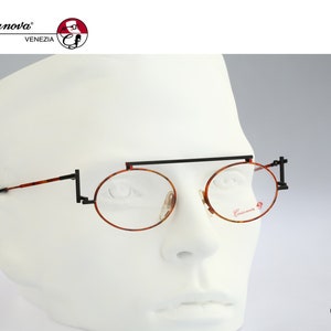 May include: A pair of round, tortoiseshell eyeglasses with a black metal frame and a thin black bar connecting the lenses. The glasses are on a white mannequin head. The brand name "Casanova" is visible on the right lens.