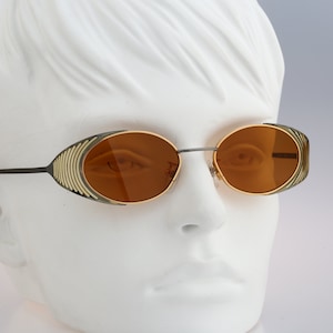 Peut inclure: Lunettes de soleil ovales avec une monture dorée et noire et des verres bruns.