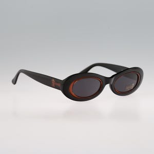 May include: Black oval sunglasses with brown frames. The sunglasses have a dark lens.