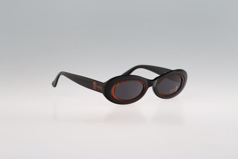 May include: Black oval sunglasses with brown frames. The sunglasses have a dark lens.