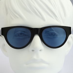 Könnte beinhalten: Schwarze Cat-Eye-Sonnenbrille mit blauen Gläsern. Die Sonnenbrille sitzt auf einem weißen Mannequin-Kopf.