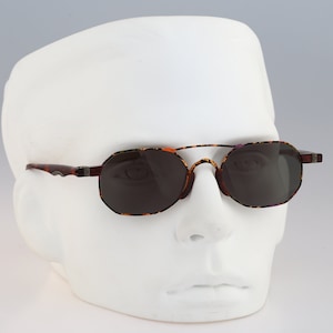 Puede incluir: Gafas de sol con montura de carey y lentes grises oscuras. Las gafas tienen un puente de metal y un acento plateado en las patillas.