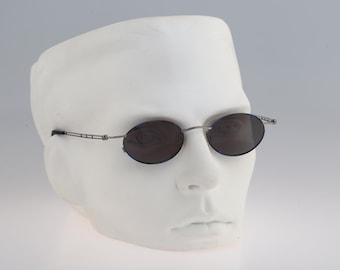 Puede incluir: Gafas de sol ovaladas plateadas con lentes grises oscuros. Las gafas están en una cabeza de maniquí blanca.