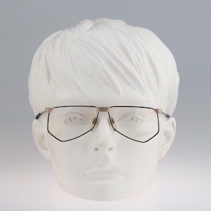 May include: A pair of gold-rimmed glasses with black frames and clear lenses. The glasses are on a white mannequin head.