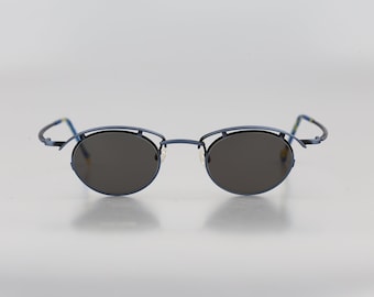 Puede incluir: Un par de gafas de sol con montura de metal azul y lentes de forma ovalada. Las lentes son de color gris oscuro.