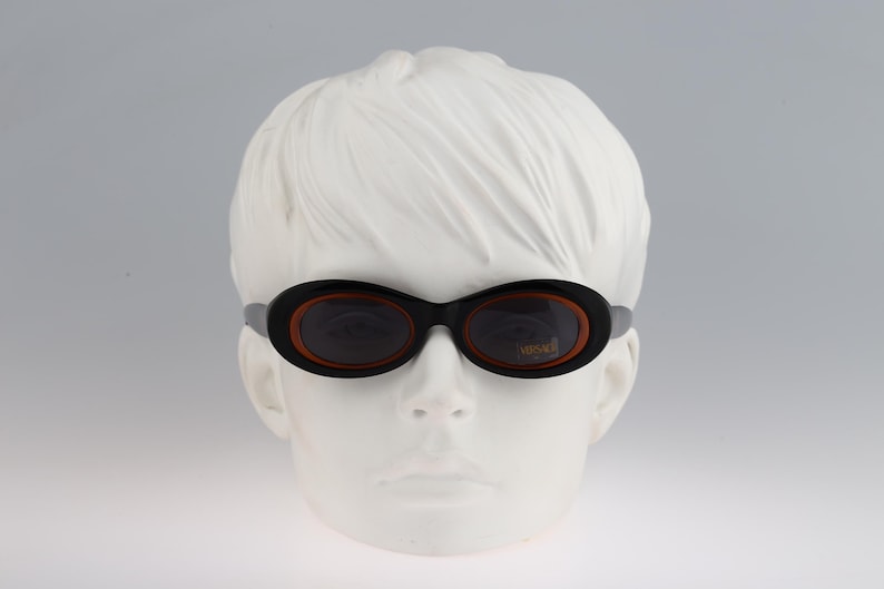 May include: A pair of black oval-shaped sunglasses with brown frames and dark lenses. The sunglasses are on a white mannequin head.