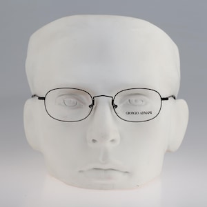 Puede incluir: Gafas rectangulares negras con un fino marco negro. El marco tiene el texto "Giorgio Armani" impreso en la lente derecha.