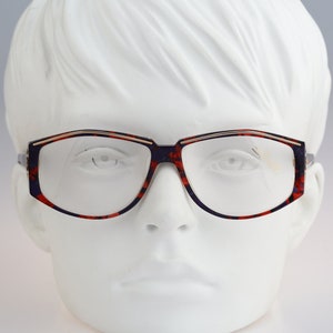 Könnte beinhalten: Eine Brille aus Schildpatt mit goldfarbenem Rand. Die Brille hat eine rechteckige Form und befindet sich auf einem weißen Mannequin-Kopf.