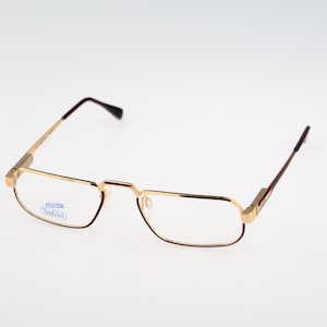 May include: Gold-tone metal eyeglasses with brown temples and clear lenses. The left lens has a blue sticker with the text "elasta Safilo".