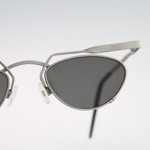 May include: A pair of silver-toned metal sunglasses with dark gray lenses. The sunglasses have a unique, angular design with a thin metal frame.
