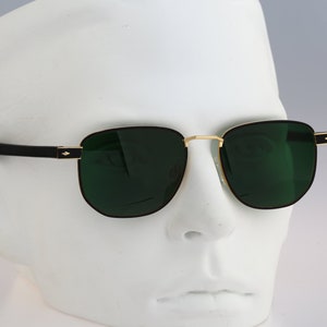 Puede incluir: Gafas de sol aviador negras y doradas con lentes verdes. Las gafas están en una cabeza de maniquí blanca.