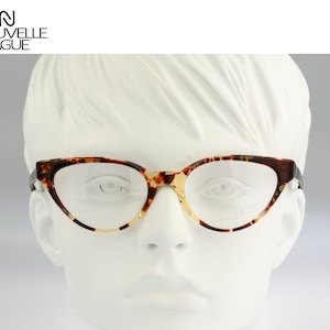 May include: Cat-eye glasses with a brown and tan tortoiseshell pattern frame. The glasses feature clear lenses and are displayed on a white mannequin head. The text NOUVELLE VAGUE is visible at the top left, and CARETTA VINTAGE is at the bottom right.