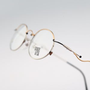 May include: Gold-rimmed round eyeglasses with clear lenses. The frame has the words "Dolce Vita" printed on the right lens.