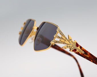 Könnte beinhalten: Goldfarbene Sonnenbrille mit einem Schildpattgestell und einem mit Kristallen besetzten Design an einem Bügel.