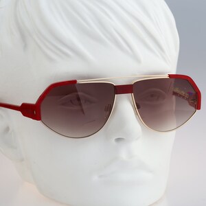 May include: Red and gold aviator sunglasses with brown lenses. The sunglasses have a unique, angular shape.