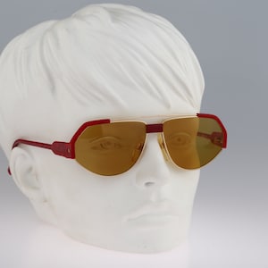 May include: Red and gold aviator sunglasses with brown lenses. The sunglasses are on a white mannequin head.