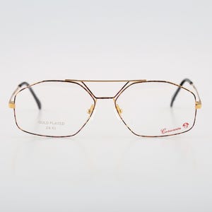 Puede incluir: Gafas de oro chapado con montura marrón y lentes transparentes. La montura tiene el texto "GOLD PLATED 24 KT" y "Caravelle" en las patillas.