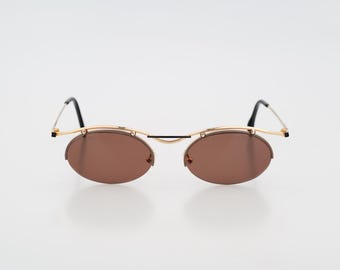 May include: Oval-shaped sunglasses featuring brown tinted lenses and a thin gold-tone metal frame. The design includes a straight gold bridge across the top, thin gold temples, and black temple tips. The lenses are secured to the frame by small screws.