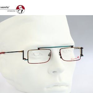 May include: A pair of red, gold, and teal eyeglasses with a black frame. The glasses have a rectangular shape and are on a white mannequin head. The brand name "Casanova" is visible on the right lens.