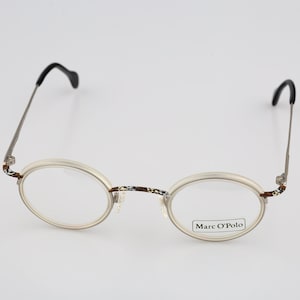 May include: Marc O'Polo eyeglasses featuring round, off-white frames with a brown and white patterned bridge and hinge accents. The thin metal temples are finished with black curved tips, and the right lens displays the Marc O'Polo brand name.