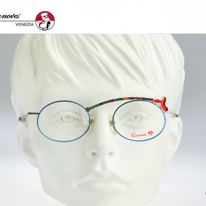 Può includere: Occhiali rotondi con montatura blu, ponte colorato e dettagli rossi. Gli occhiali sono su una testa di manichino bianca.