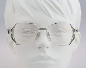 May include: Silver-toned metal eyeglasses featuring a distinct octagonal frame shape. The glasses have clear lenses and thin, polished silver temples. The outer edges of the frames are accented with a textured, dark green and black mottled pattern.
