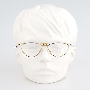 May include: Gold-rimmed eyeglasses with a cat-eye shape. The frames have a tortoiseshell pattern on the upper rims and temples. The glasses are displayed on a white mannequin head against a white background.