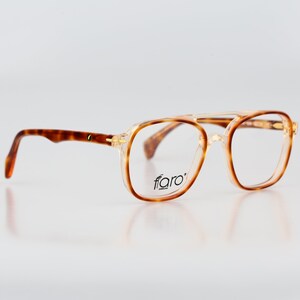 May include: Tortoise shell eyeglasses with gold accents and a clear lens. The brand name "fiaro" is printed on the frame.