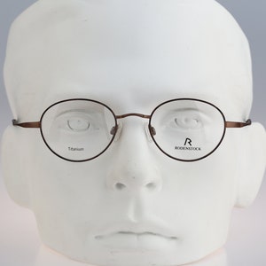 Op de afbeelding: Bruine ronde bril met een titanium montuur en de tekst "R RODENSTOCK" op de rechter lens.