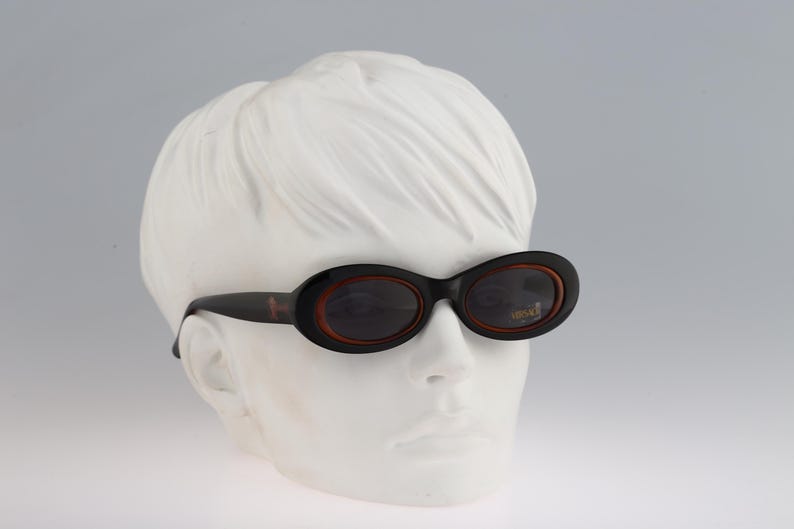 May include: A pair of black oval sunglasses with brown frames. The sunglasses are on a white mannequin head.