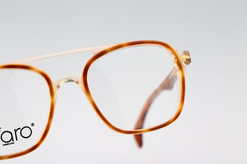 May include: Close-up of a pair of tortoiseshell eyeglasses with a gold metal bridge. The glasses have a clear lens and the brand name "faro" is printed on the left temple.