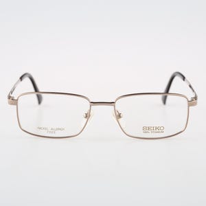 Può includere: Occhiali rettangolari con montatura in metallo color bronzo e terminali delle aste neri. Le lenti presentano la scritta stampata SEIKO 100% TITANIUM e NICKEL ALLERGY FREE. Questi occhiali hanno naselli regolabili e una struttura sottile.