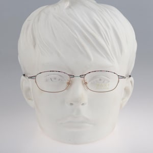 May include: A pair of rimless eyeglasses with a rose gold frame and light blue accents. The glasses are on a white mannequin head.