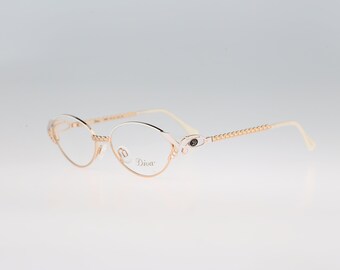May include: Gold-tone metal spectacles with oval-shaped frames. The temples feature a textured chain-link design. The right lens is etched with the word Diva. The bridge and hinges have a polished finish, and the temple tips are a light cream colour.