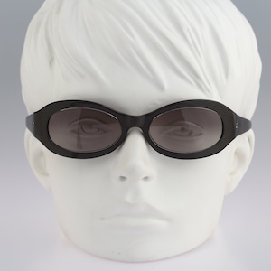May include: Black oval sunglasses with dark lenses on a white mannequin head.