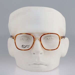 May include: Brown tortoiseshell eyeglasses with a square frame and clear lenses. The glasses have the word "faro" printed on the right lens.