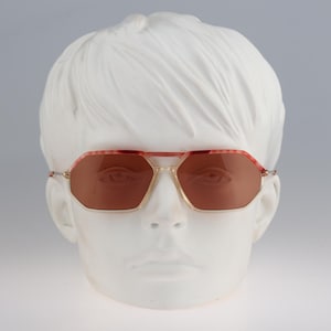 Puede incluir: Un par de gafas de sol de forma octogonal de color rojo y dorado con lentes marrones.