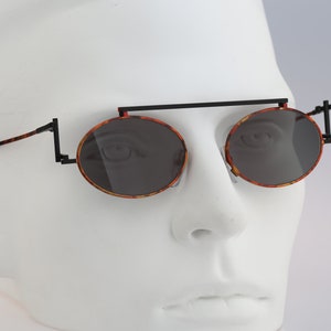 May include: Round tortoiseshell sunglasses with black metal frames and a black bar connecting the lenses.