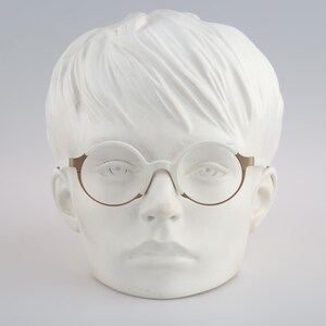 May include: A white mannequin head wearing round, clear-framed glasses with a gold metal frame.
